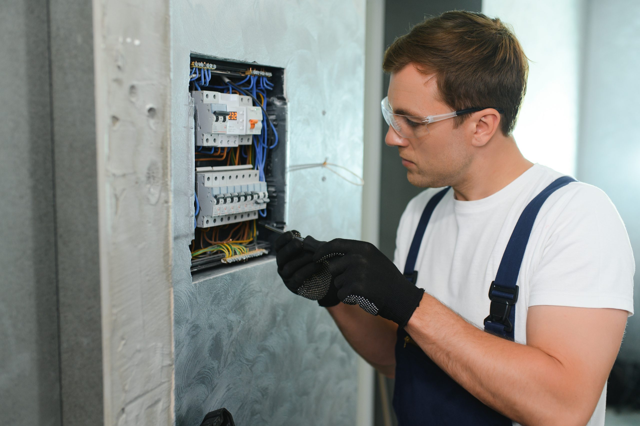 A male electrician works in a switchboard with an electrical connecting cable